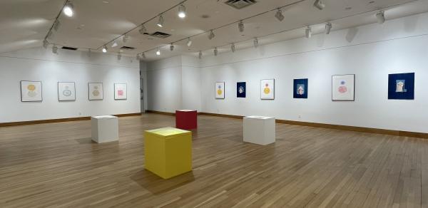 gallery with artwork on the walls and colored plinths in the center of the space.