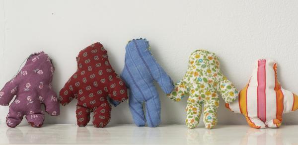 Photograph of 5 sculptures. Each sculpture is a small doll looking entity. Each is made of a different color fabric with patterns. 