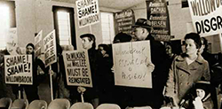 Families protest Willowbrook conditions in 1971. Their large painted signs read, “Shame! Shame! Willowbrook” and “Dr. Wilkins and Mrs. Lee MUST BE REINSTATED.” One hand-written sign says “Willowbrook Escuela o Prisión (‘Willowbrook School or Prison’)”