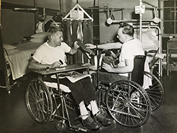 Two Halloran Hospital patients in wheelchairs. They make weight belts as part of their physical and occupational rehabilitation following injuries sustained in battle. This image appeared in the Halloran Beacon, the hospital’s magazine.