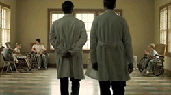 In this still shot from the film Willowbrook (2012), two doctors walk through a research ward with well-clothed patients and clean, calm surroundings, ostensibly made possible through funding for unethical research that harmed children. 