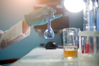 Gloved hand in a lab holds up a beaker full of liquid