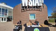 3 people sitting at the table with Green Club Logo in front of the building with WSIA 88.9fm sign