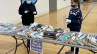 2 kids standing next to  tables  with books