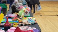 2 people standing next to tables with children clothing and toys