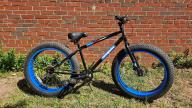A Mongoose branded black and blue bike with large black wheels, black seat,  with handbreaks and gears
