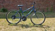 A Huffy branded dark blue bike with a black seat, slightly curved handle bar and, black wheels with handbreaks and gears 