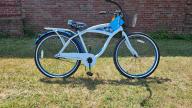 A Margaritaville branded white - framed bike with black handlebars, a black basket, a cup holder, pedal breaks, and a white and navy blue palmtree - decorated seat.