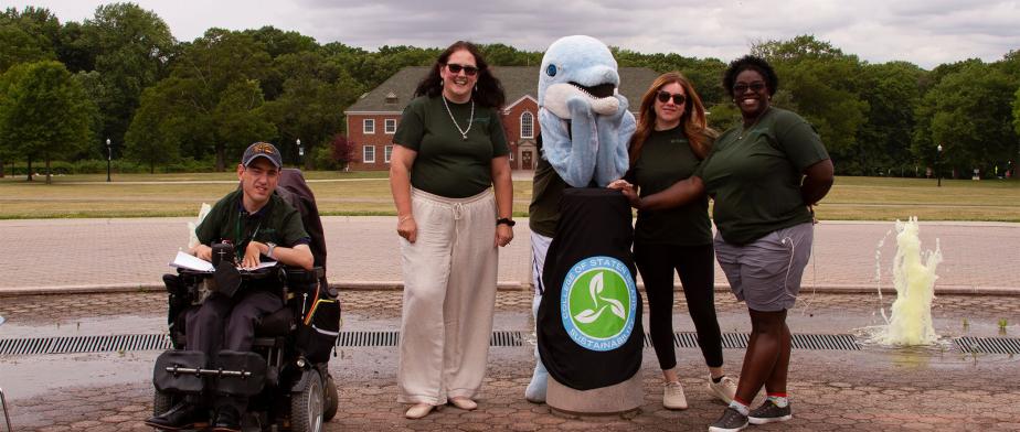 4 people with CSI mascot dolphin in front of the fountain