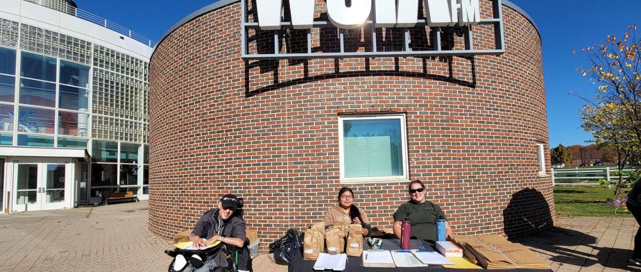 Composting workshop with compost and leaf bag giveaway 3 people sitting at the table with Green Club Logo in front of the building with WSIA 88.9fm sign