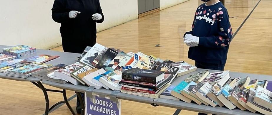 2 kids standing next to  tables  with books