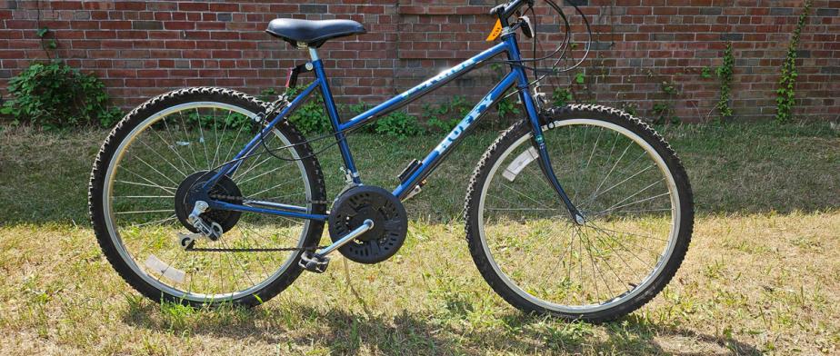 A Huffy branded dark blue bike with a black seat, slightly curved handle bar and, black wheels with handbreaks and gears 