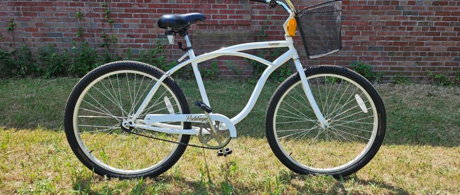 15. Cruiser A Radeberger Pilsner white bike with a black seat, with gears, black wheels, curved handle bars and pedal breaks