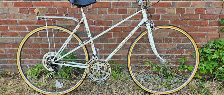 A white Peugeot branded bike with yellow rims, rear rack, gears and a handle break