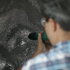 Miguel A. Aragon working in the studio Artist using a hand-drill to pierce through paper