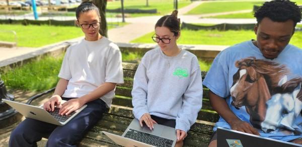 Three Students Sitting on a Campus Bench Working on Laptops