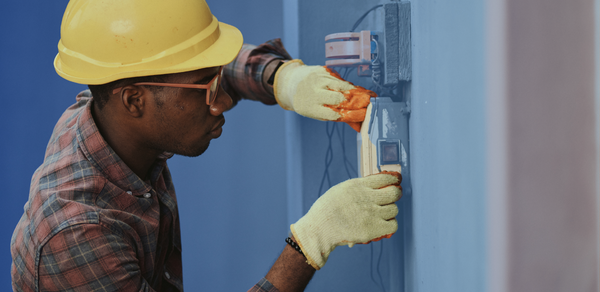 Man in glasses and yellow hard hat working on electrical circuit on wall