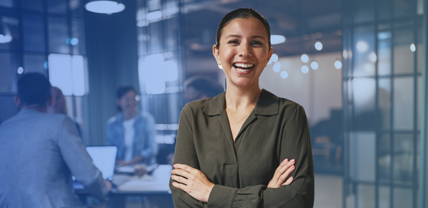 Young woman smiling in office with employees having a meeting behind her