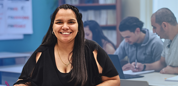 Young woman smiling in classroom with students working together behind her