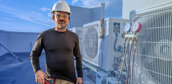 Man wearing white hard hat on roof standing beside industrial air conditioning unit