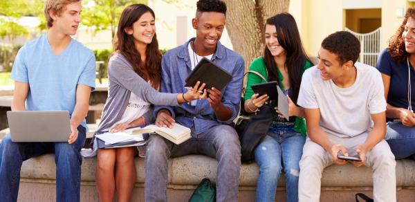 students looking at laptop outdoors by tree