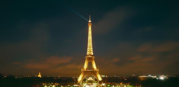 The Eiffel Tower illuminated at night, with a golden glow and a sparkling light show