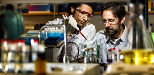 2 male students with beakers in a lab.