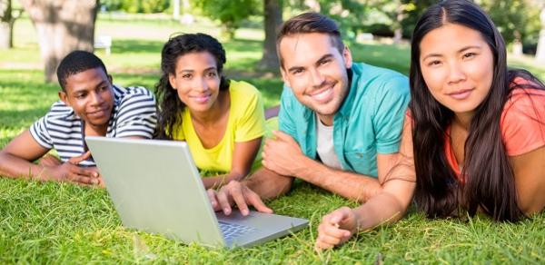 Four student looking at a laptop while lying down in a grassy field