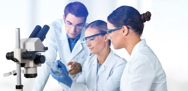 Three Students In Labcoats Looking At Microscope