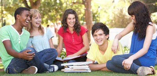 A group of five students sitting outside on the grass surrounded by a stack of books