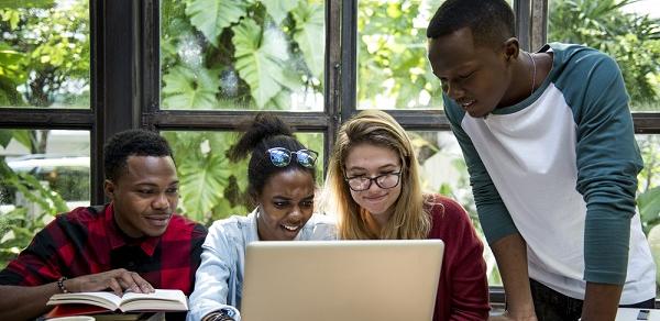 A group of four students huddled around a laptop