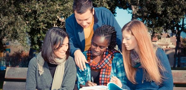 Students Huddled In A Group Looking Down At Book