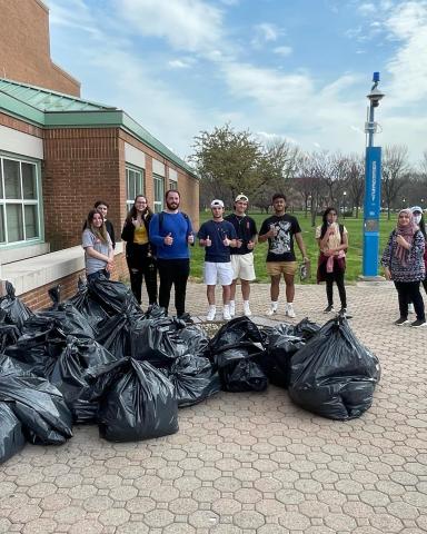 Students standing in front of 1P after finishing the Campus Clean Up. There are 20+ black garbage bags in front of them on the floor. ​