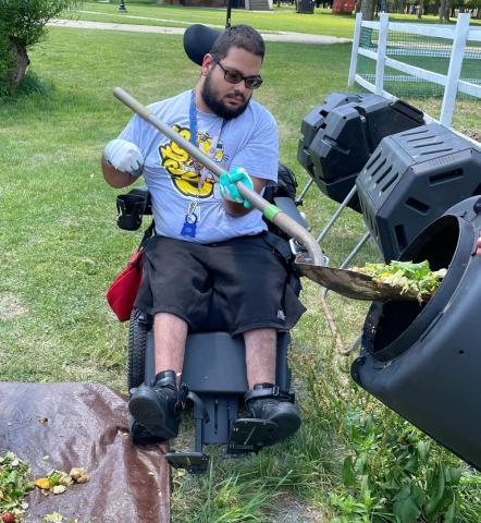 Composting workshop 1 student in a wheelchair is lifting up the pre-consumer waste to be placed in the composter.