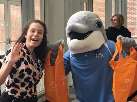 CSI's mascot Danny the dolphin is standing with visitor holding an orange reusable bag​