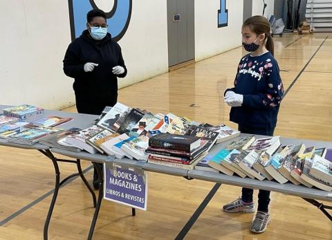 2 kids standing next to  tables  with books