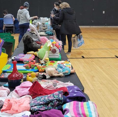 2 people standing next to tables with children clothing and toys