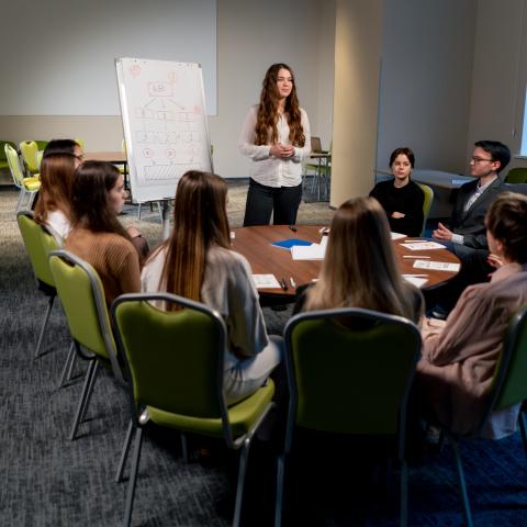 group of people sitting around the table looking at a presenter in front of a white board