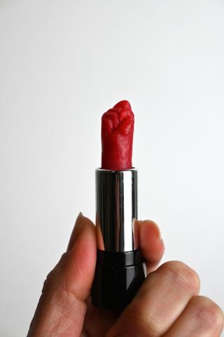 a woman's hand holds an open lipstick carved in the shape of an upraised fist